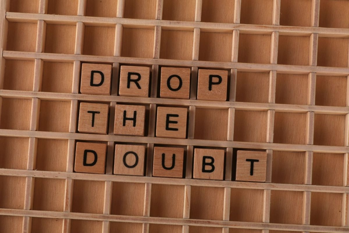 Wooden letter tiles spelling 'Drop the Doubt' on a wooden grid background, promoting positivity.