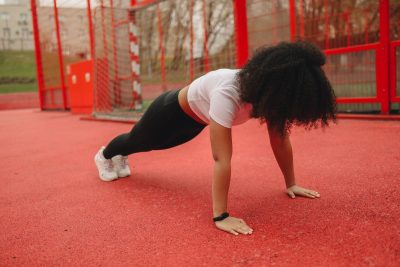 African American woman doing planks outdoors on a red sports track. Promoting a healthy lifestyle.